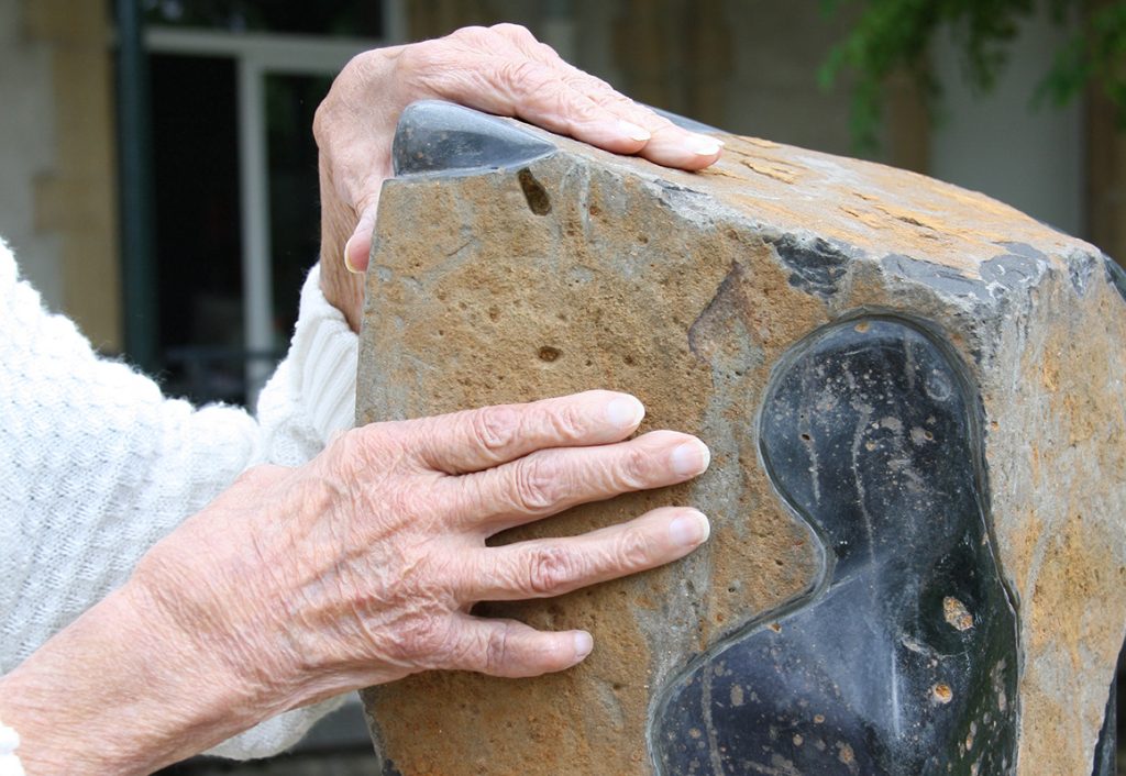 un patient touche une sculpture en pierre du jardin thérapeutique