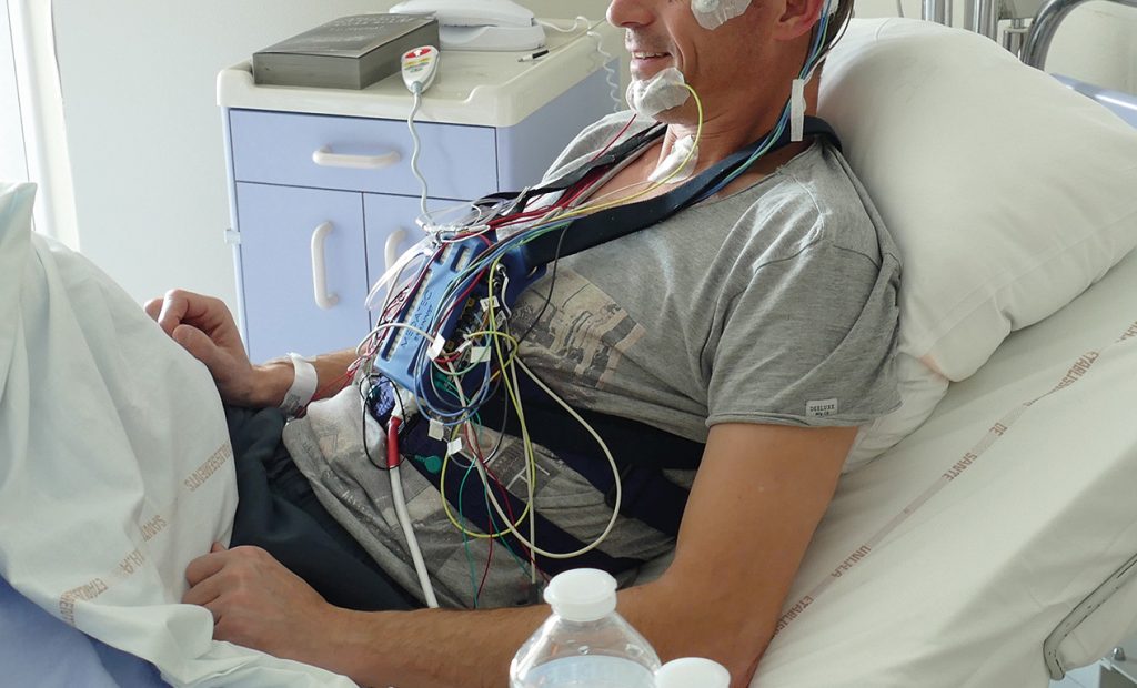 Photo d'un patient équipé du dispositif de polysomnographie et installé dans sa chambre d'hospitalisation