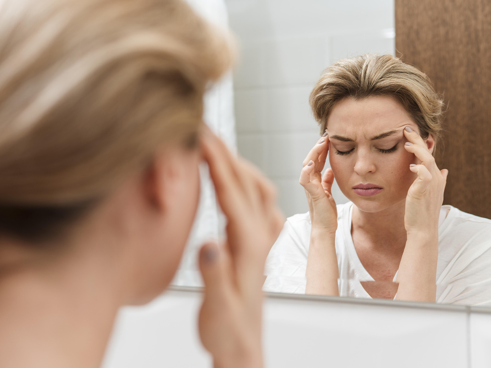 femme avec un mal de crâne face au miroir
